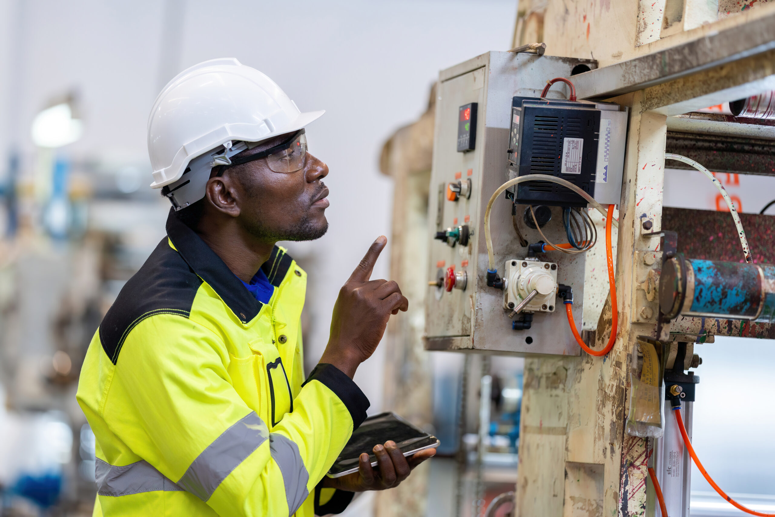 african male engineer department head point to the electronic circuit board. of machinery in plastic and steel industries wear a safety helmet and vest. holding laptop to work